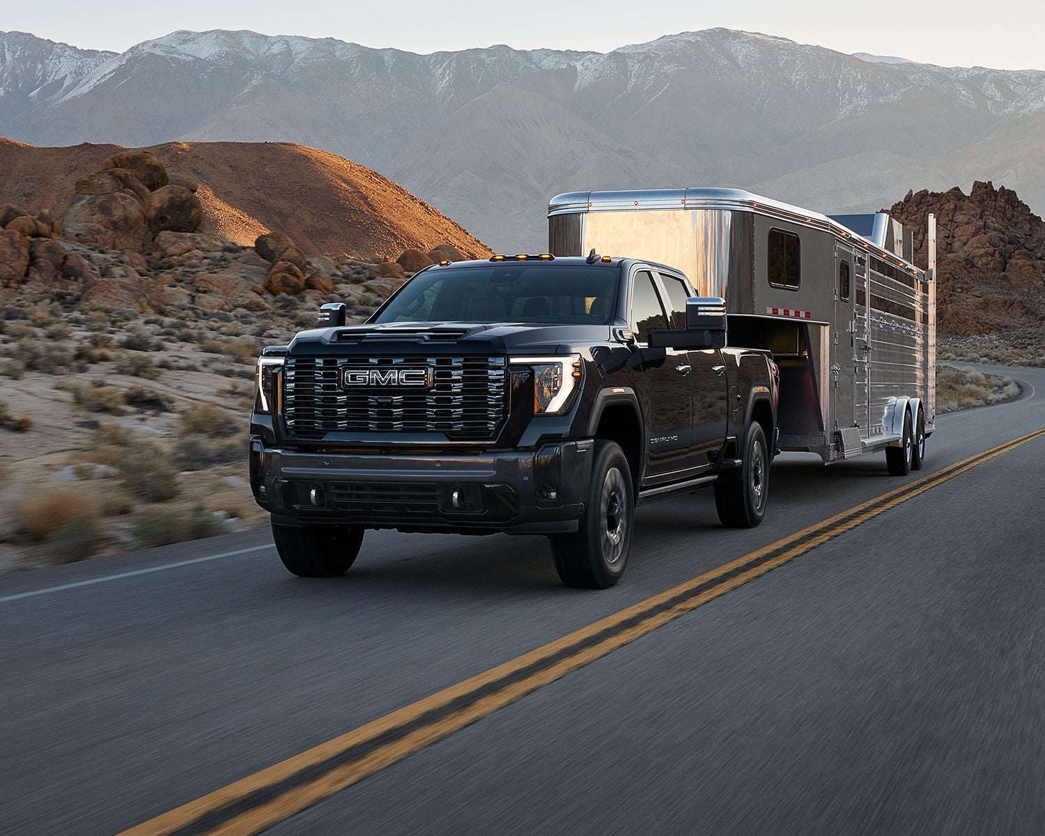 Front 3/4 shot of the 2025 GMC Sierra HD towing a trailer on a road.