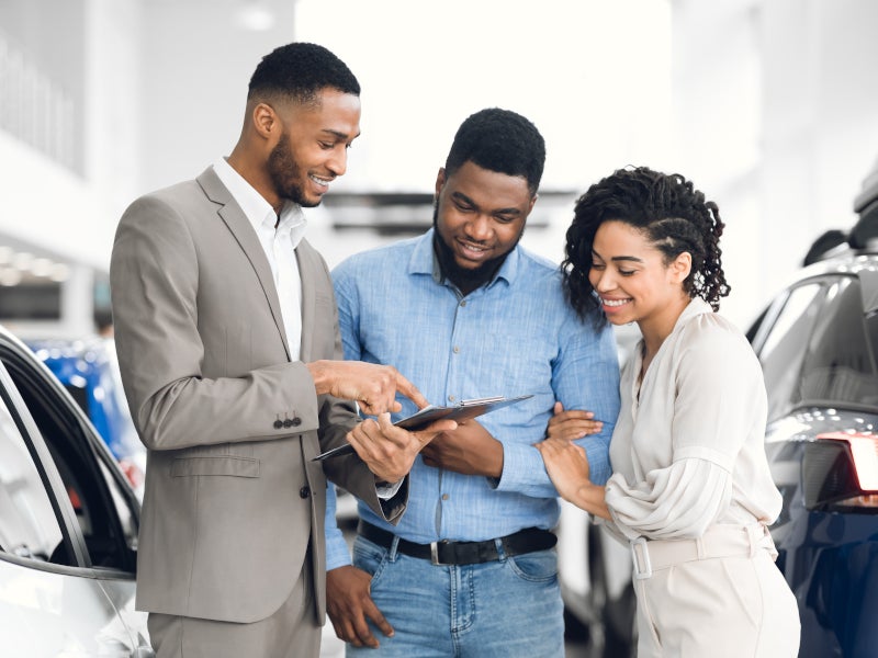 salesperson showing customers a new car at a dealership